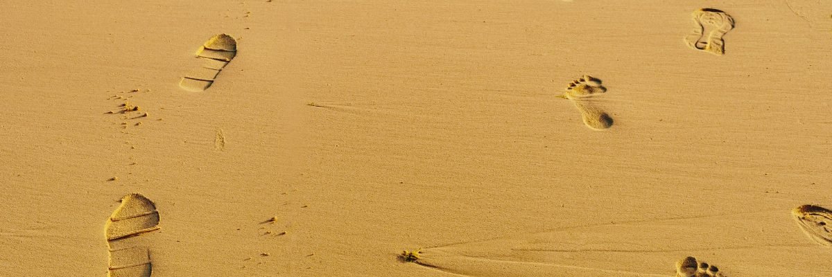 Empreintes de pas humains laissées sur une plage de sable doré, de différentes formes et profondeurs