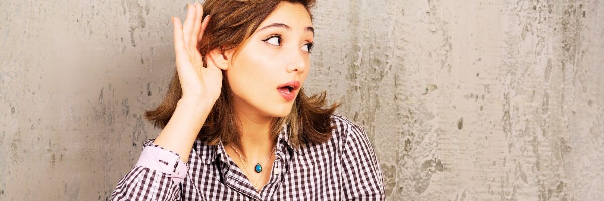 Femme écoutant attentivement avec la main derrière l’oreille, symbolisant l’écoute du langage du corps et des signaux subtils.