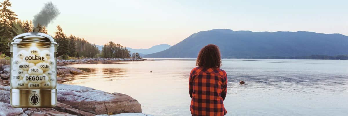 Silhouette de dos assise face à un lac et à une montagne au lever du soleil, avec à côté une cocotte-minute en verre laissant s’échapper une vapeur noire symbolisant les émotions en quarantaine comme la peur, la colère ou la tristesse.