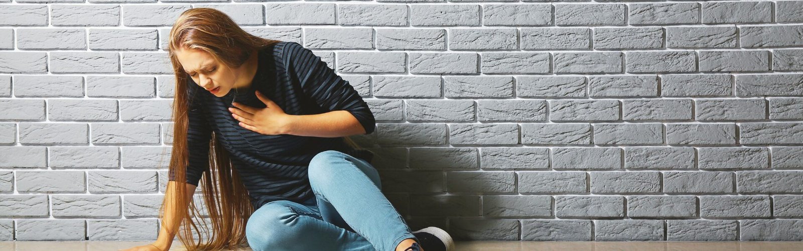 Femme assise au sol, la main sur la poitrine, en pleine crise d’angoisse qui surgit soudainement.