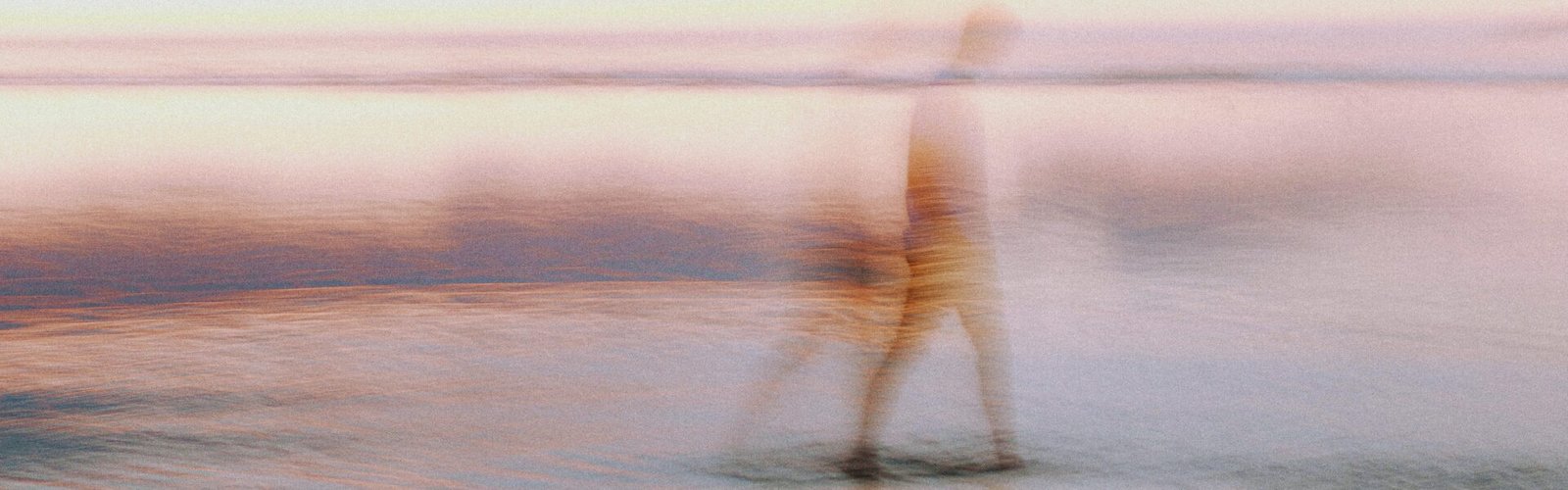 Silhouette masculine floue marchant sur une plage, les pieds dans l’eau, avec un effet artistique de dissolution et de flou, symbolisant la fatigue de l’âme et le poids invisible des émotions.