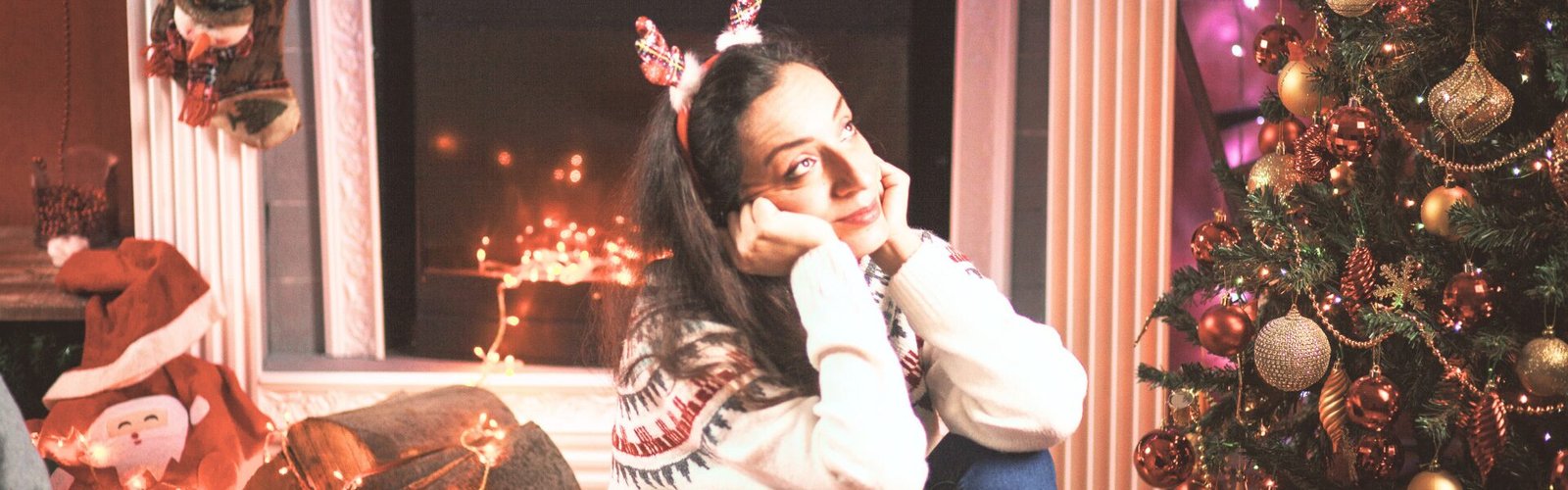 personne assise près d’un sapin de Noël, entourée de lumières, le regard pensif et ailleurs