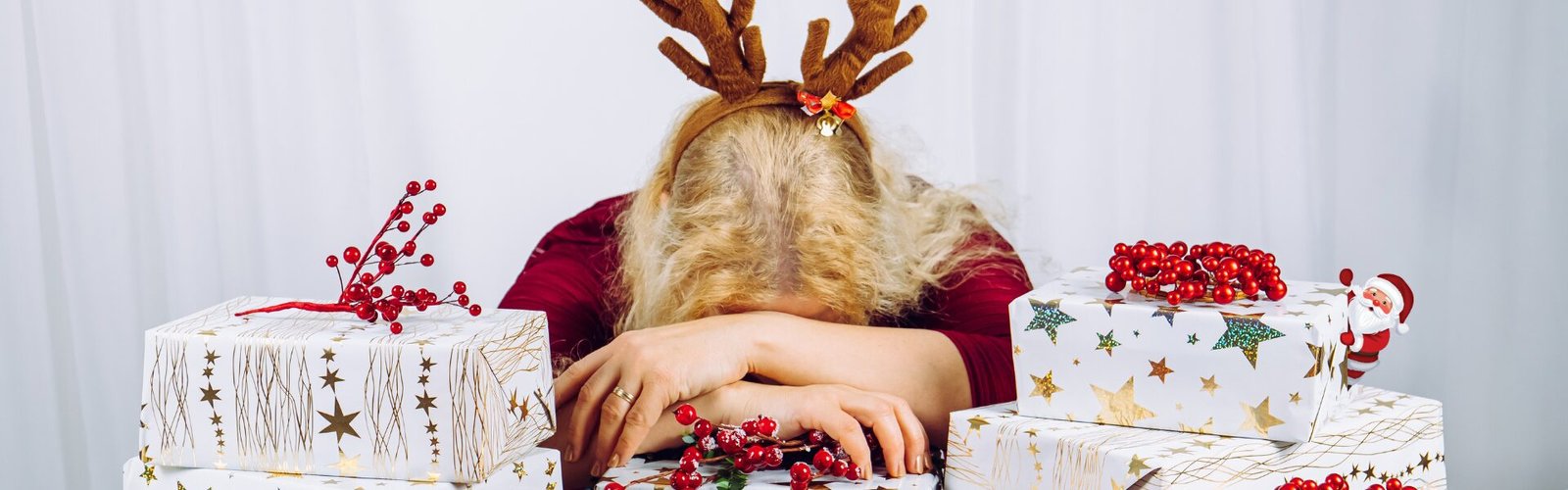 Femme fatiguée, tête posée sur les bras, entourée de cadeaux, illustrant la fatigue émotionnelle ressentie à l’approche de Noël