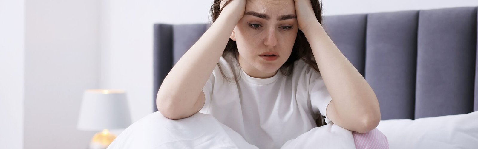 Femme préoccupée assise dans son lit illustrant le manque de libido chez la femme.