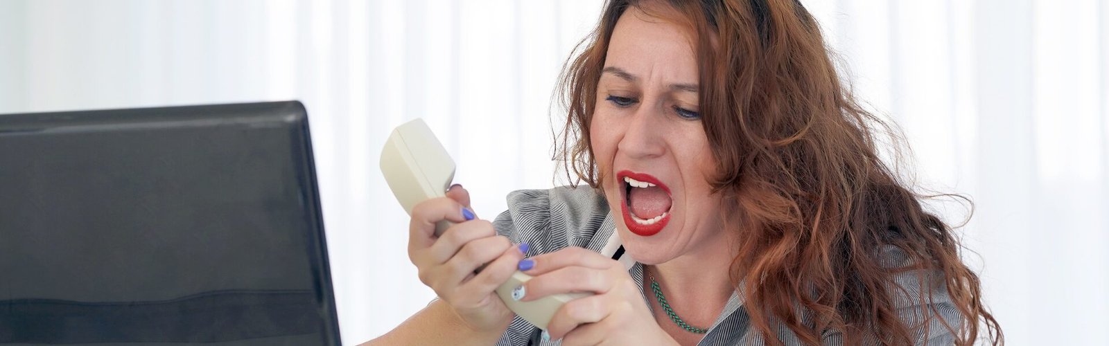 Femme assise devant un ordinateur, exprimant une colère intense au téléphone, illustrant une réaction disproportionnée à un message ou une situation.