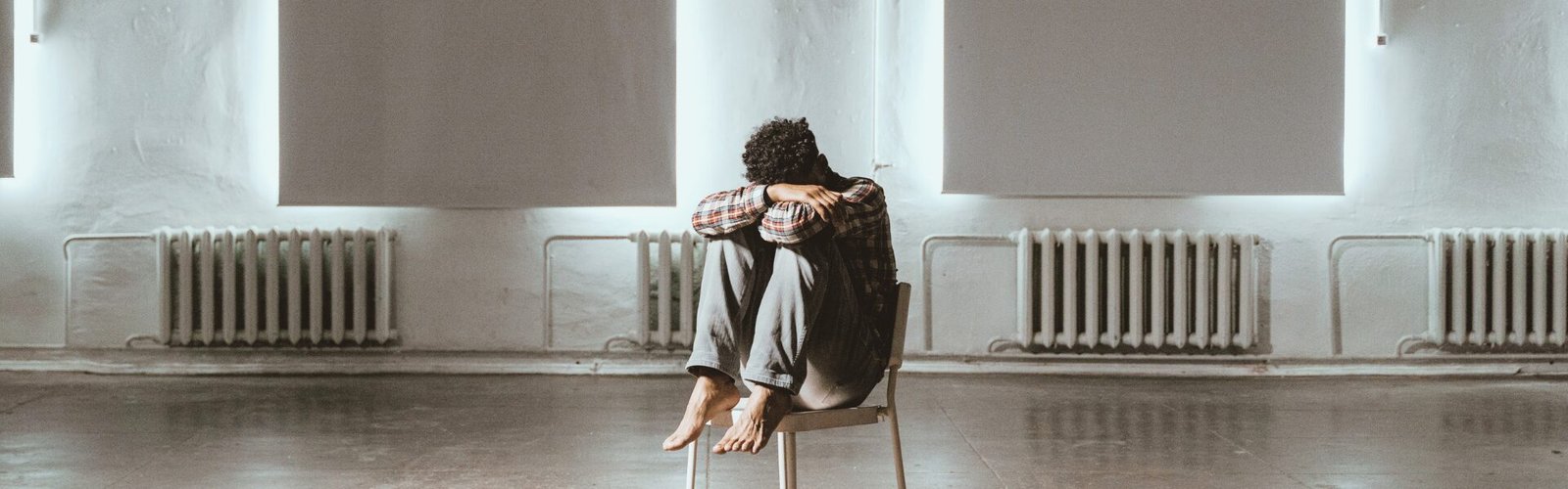 Personne assise seule dans une pièce vide, posture fermée, illustrant la peur du changement et le blocage intérieur