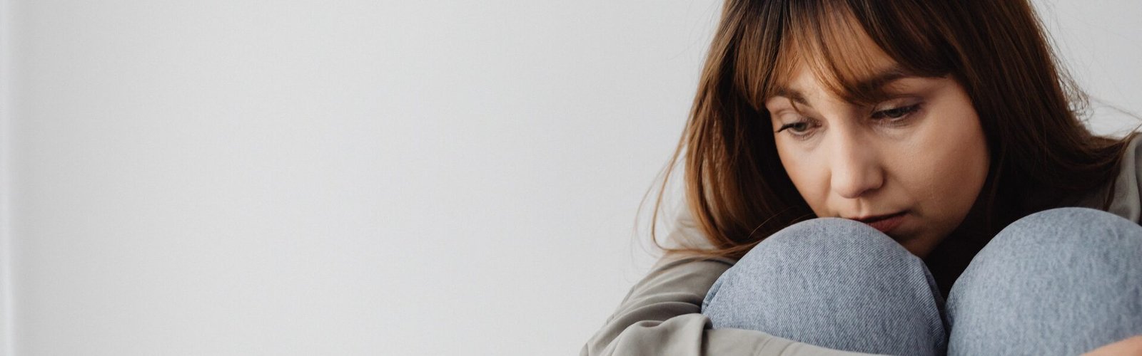 Femme assise recroquevillée, les bras entourant ses genoux et la tête posée sur l’un d’eux, le regard perdu, exprimant illustrant la sensation de se sentir coupable
