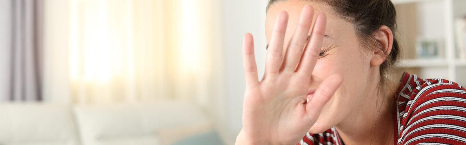 Femme levant la main devant son visage en signe de gêne ou de protection, illustrant une réaction de malaise dans une interaction sociale.