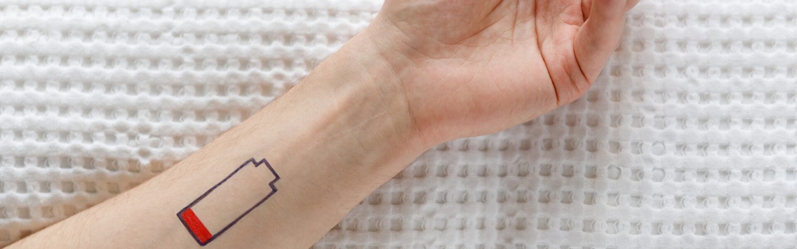 Avant-bras avec un symbole de batterie faible illustrant la fatigue et l'épuisement liés aux douleurs chroniques.